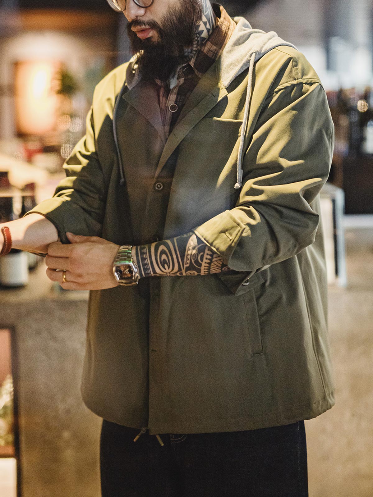 詳細画像
「耐久性に優れたヘリンボーン生地とヴィンテージ感を引き立てるレーザーボタン、明るいステッチラインのディテールをクローズアップした画像。」
モデル画像
「モデルがレイヤード風 パッチワーク フード付きワークジャケットを着用し、レトロなワークウェアと現代のアーバンスタイルを融合したコーディネートを披露。」