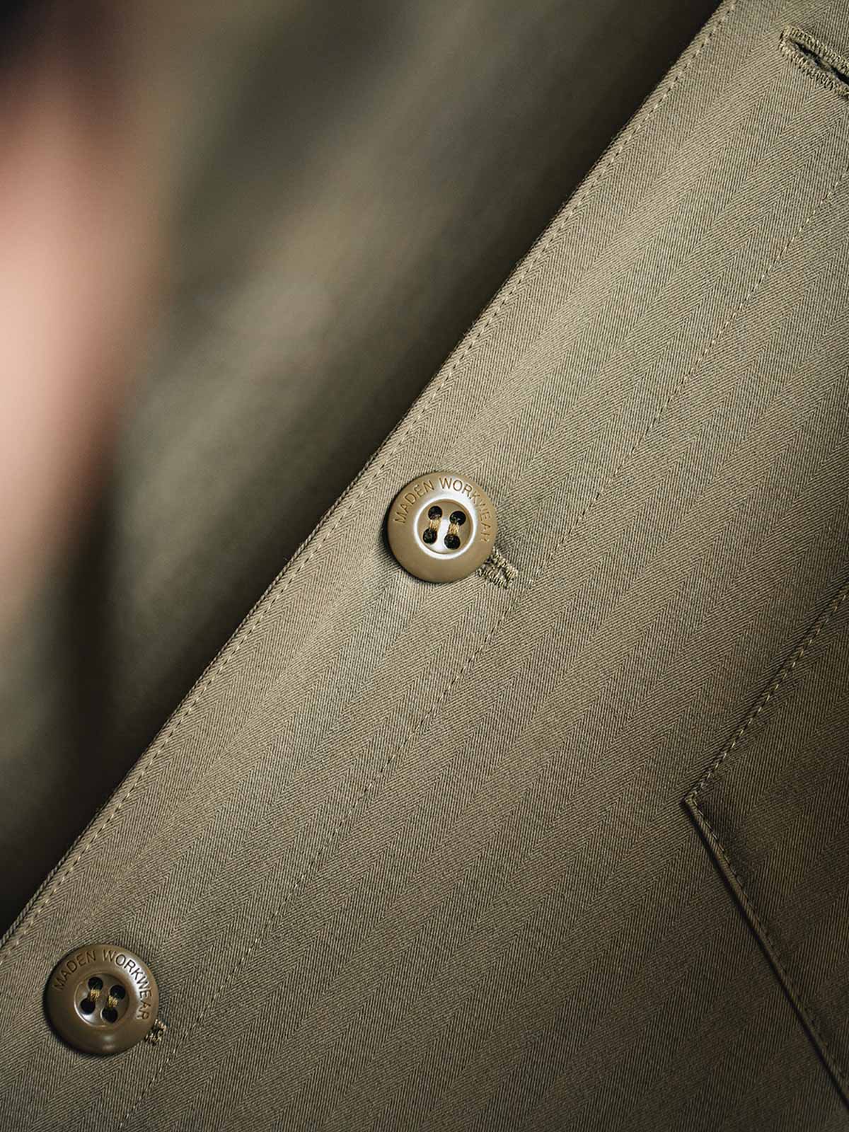 製品画像
「レイヤード風デザインのパッチワーク フード付きワークジャケット全体画像。ヘリンボーン生地と3ポケット仕様が特徴的なアーバンカジュアルアウター。」
詳細画像
「耐久性に優れたヘリンボーン生地とヴィンテージ感を引き立てるレーザーボタン、明るいステッチラインのディテールをクローズアップした画像。」