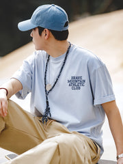 モデルが着用する「BRAVE MOUNTAIN ATHLETIC CLUB」プリントのマカロンカラーTシャツ、リラックスしつつ洗練されたフィット感を示す。