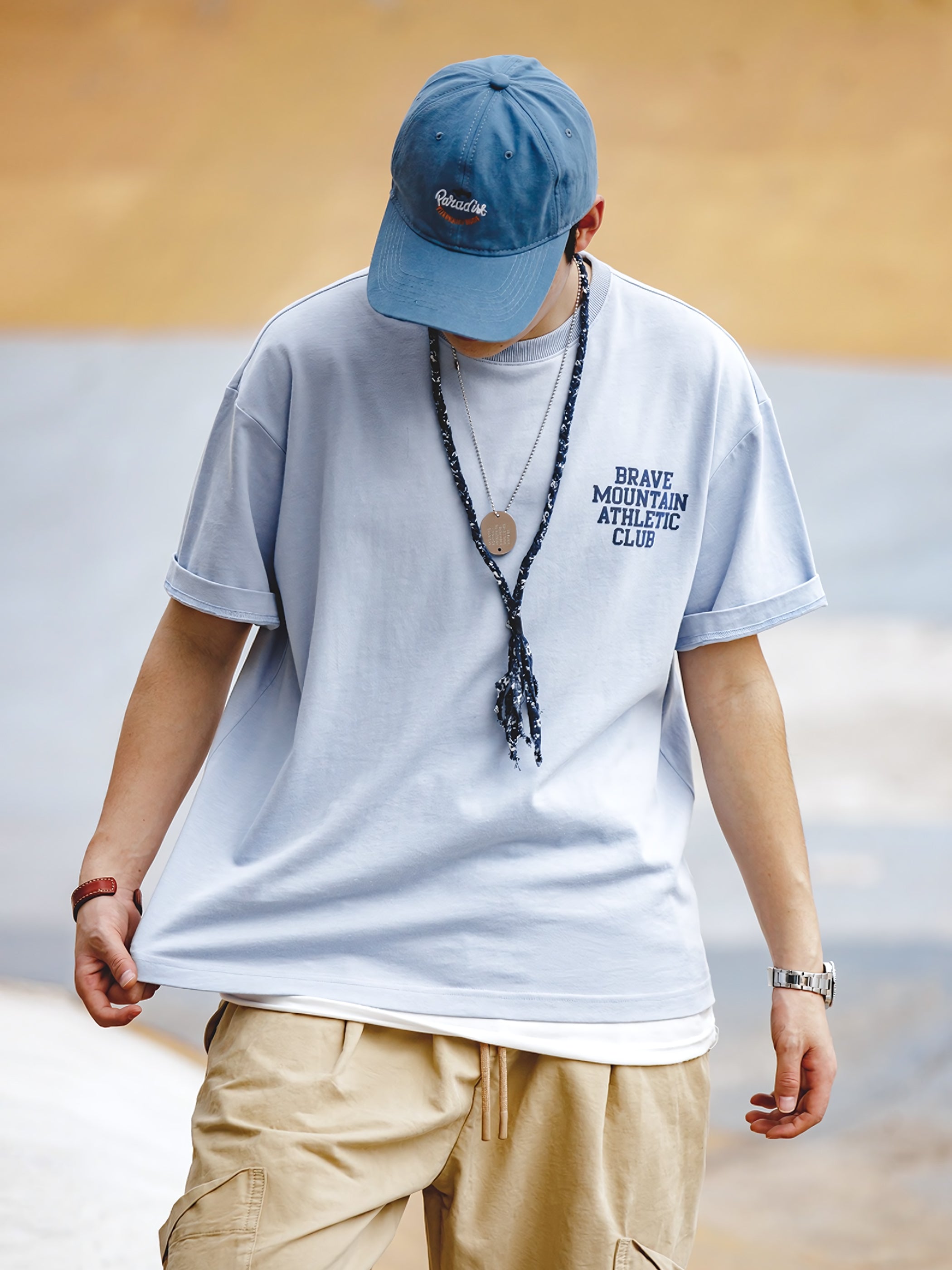 モデルが着用する「BRAVE MOUNTAIN ATHLETIC CLUB」プリントのマカロンカラーTシャツ、リラックスしつつ洗練されたフィット感を示す。