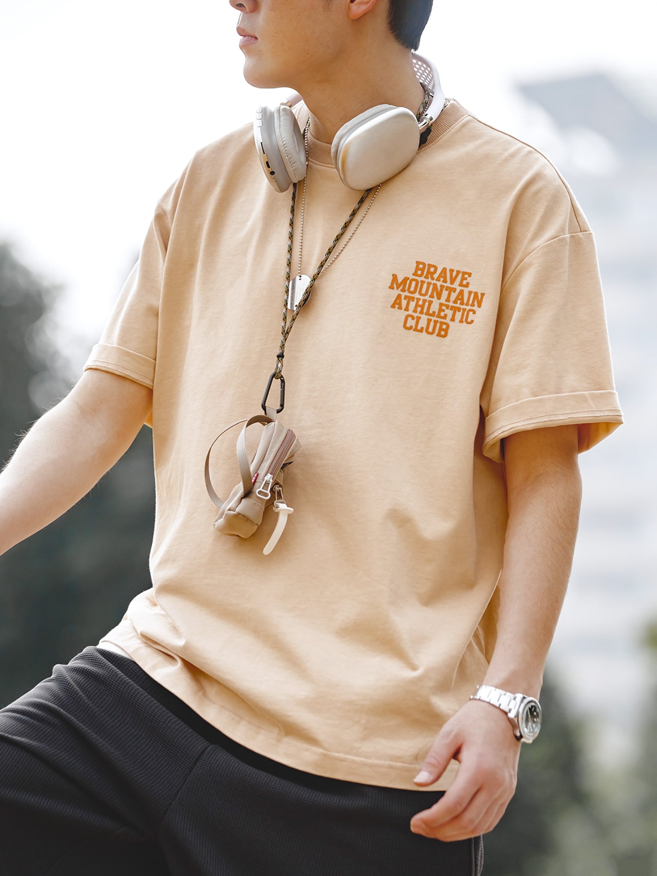 モデルが着用する「BRAVE MOUNTAIN ATHLETIC CLUB」プリントのマカロンカラーTシャツ、リラックスしつつ洗練されたフィット感を示す。