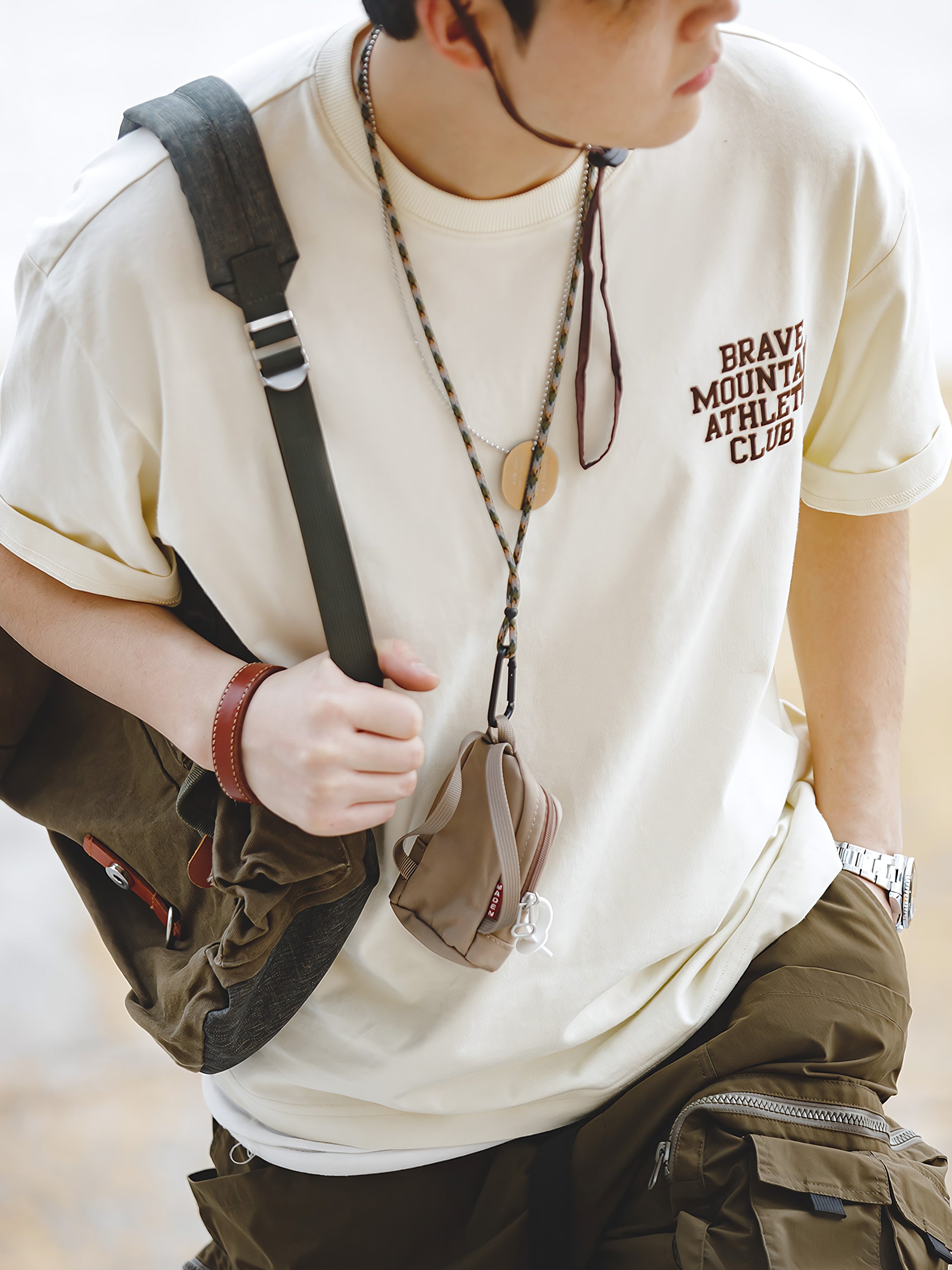 モデルが着用する「BRAVE MOUNTAIN ATHLETIC CLUB」プリントのマカロンカラーTシャツ、リラックスしつつ洗練されたフィット感を示す。