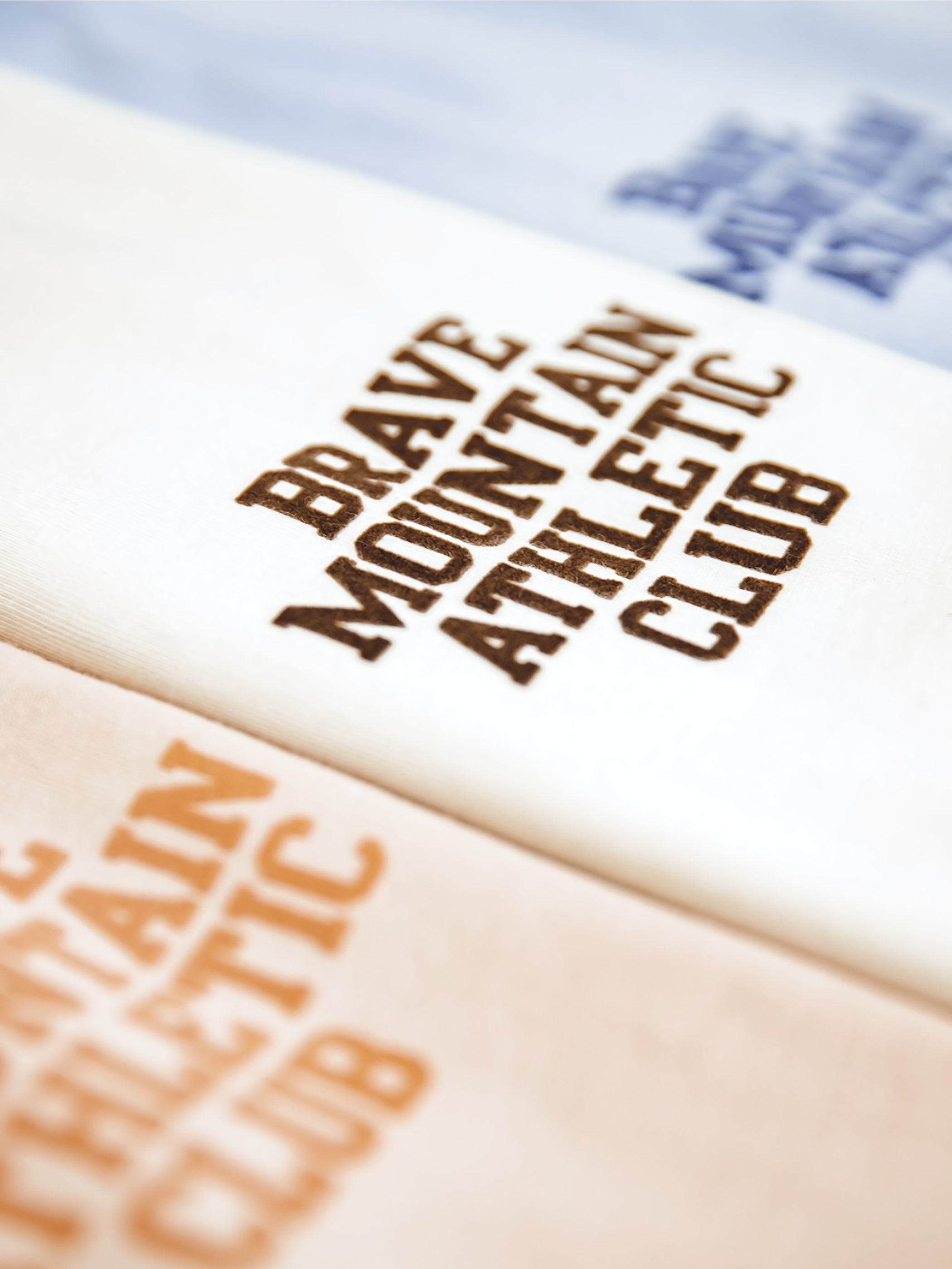 胸に「BRAVE MOUNTAIN ATHLETIC CLUB」のフロッキープリントが施されたマカロンカラーのTシャツ、100%コットン素材。