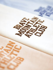 胸に「BRAVE MOUNTAIN ATHLETIC CLUB」のフロッキープリントが施されたマカロンカラーのTシャツ、100%コットン素材。