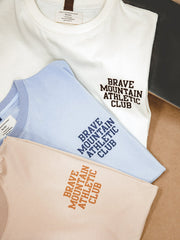 胸に「BRAVE MOUNTAIN ATHLETIC CLUB」のフロッキープリントが施されたマカロンカラーのTシャツ、100%コットン素材。