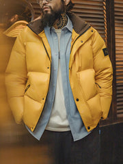 詳細画像
六角形ジッパーチャームとインディアン柄刺繍ディテール、鮮やかなイエローが際立つデザイン、防水加工されたナイロン素材とレトロなディテールのクローズアップ
モデル画像
80年代のストリートカルチャーを反映したイエローダウンジャケットを着用したモデル、高襟デザインと鮮やかなカラーが目を引く、街中のストリートスタイルを表現