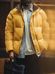 詳細画像
六角形ジッパーチャームとインディアン柄刺繍ディテール、鮮やかなイエローが際立つデザイン、防水加工されたナイロン素材とレトロなディテールのクローズアップ
モデル画像
80年代のストリートカルチャーを反映したイエローダウンジャケットを着用したモデル、高襟デザインと鮮やかなカラーが目を引く、街中のストリートスタイルを表現