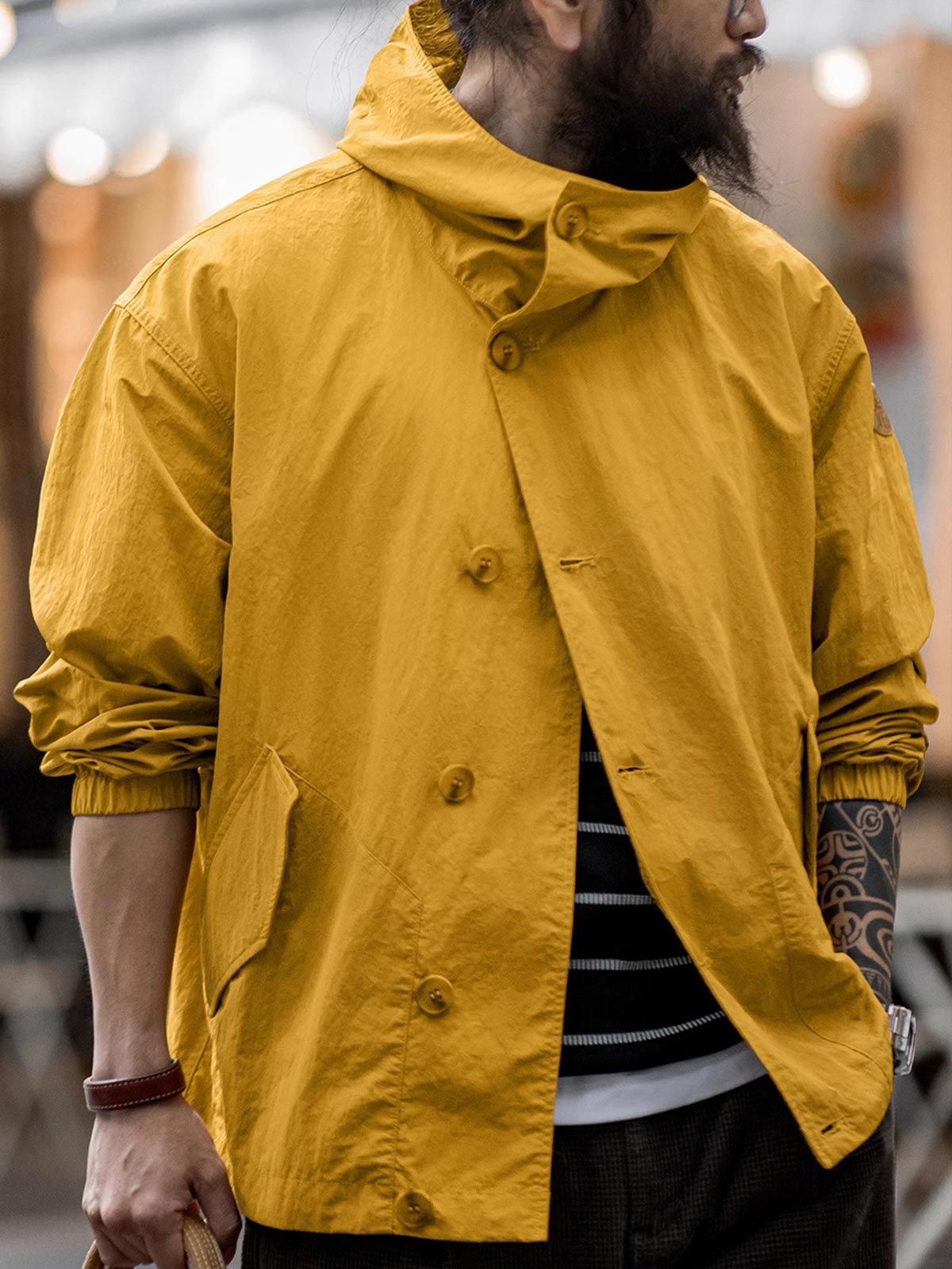 詳細画像
スタンドカラーと折り襟の2WAY仕様、エポレットディテール、フラップ付きスナップボタンポケット、そしてドローコード付き裾のディテールを強調したクローズアップ画像。機能性とデザイン性が融合した細部。
モデル画像
リラックス感のあるオーバーサイズシルエットのヴィンテージフード付きジャケットを着用し、アウトドアコーディネートを演出したモデル画像。軽量で耐久性のあるデザインが際立つスタイル。