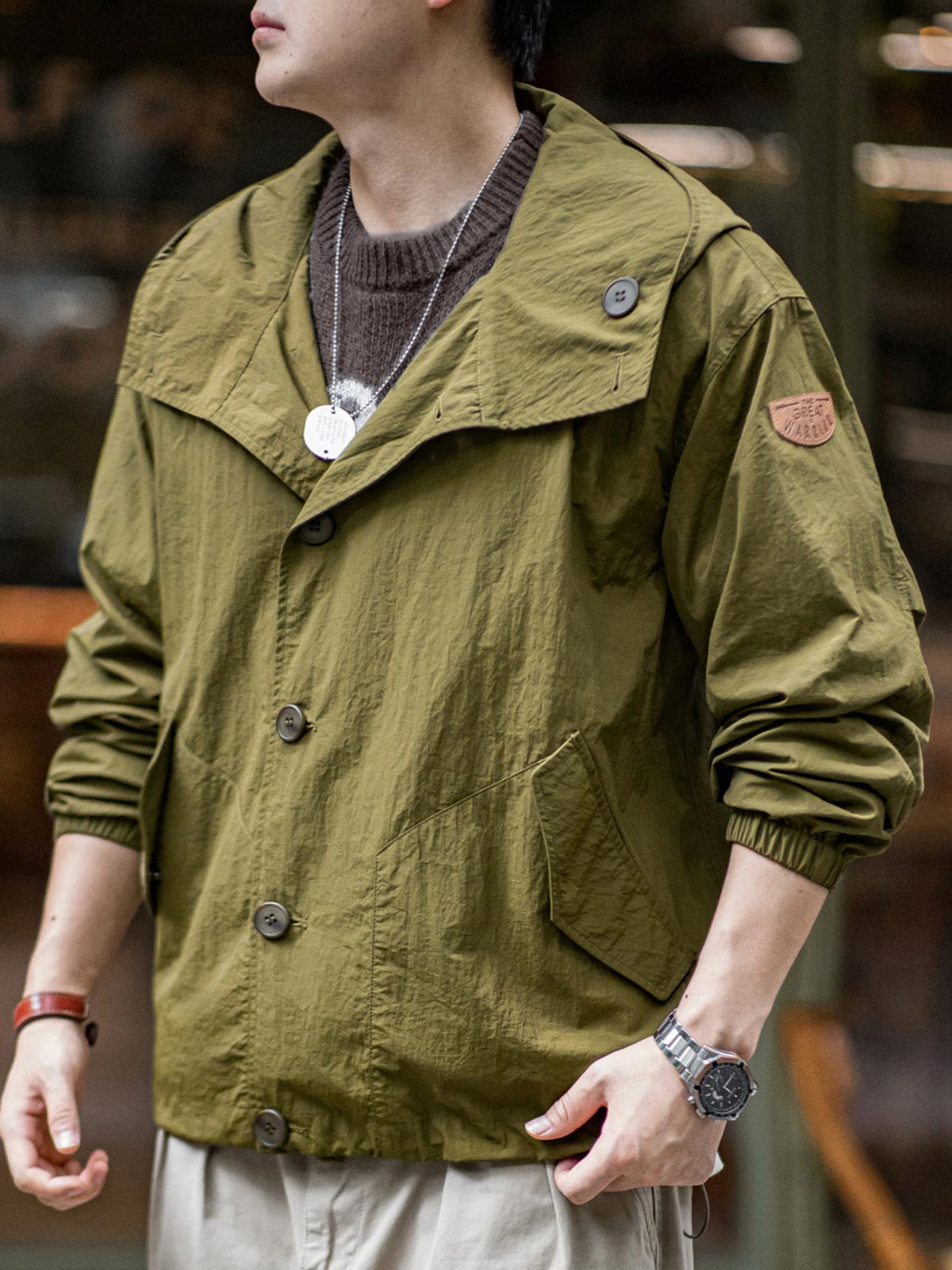 詳細画像
スタンドカラーと折り襟の2WAY仕様、エポレットディテール、フラップ付きスナップボタンポケット、そしてドローコード付き裾のディテールを強調したクローズアップ画像。機能性とデザイン性が融合した細部。
モデル画像
リラックス感のあるオーバーサイズシルエットのヴィンテージフード付きジャケットを着用し、アウトドアコーディネートを演出したモデル画像。軽量で耐久性のあるデザインが際立つスタイル。