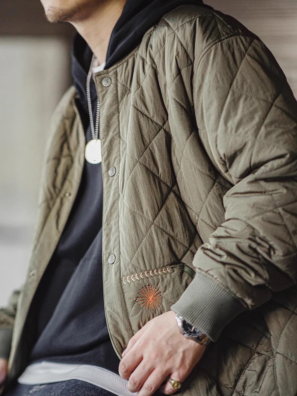 詳細画像: キルティングベースボールジャケットのステッチポケットとオレンジ色の手刺繍風ディテールのクローズアップ。銅製スナップボタンのディテールと、均等に分布した中綿が暖かさを保証。
モデル画像: モデルがキルティングベースボールジャケットデザイン中綿ジャケットを着用している画像。レトロなスタイルと現代的な技術を融合したデザインで、秋冬のカジュアルコーディネートにぴったり。