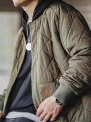 詳細画像: キルティングベースボールジャケットのステッチポケットとオレンジ色の手刺繍風ディテールのクローズアップ。銅製スナップボタンのディテールと、均等に分布した中綿が暖かさを保証。
モデル画像: モデルがキルティングベースボールジャケットデザイン中綿ジャケットを着用している画像。レトロなスタイルと現代的な技術を融合したデザインで、秋冬のカジュアルコーディネートにぴったり。