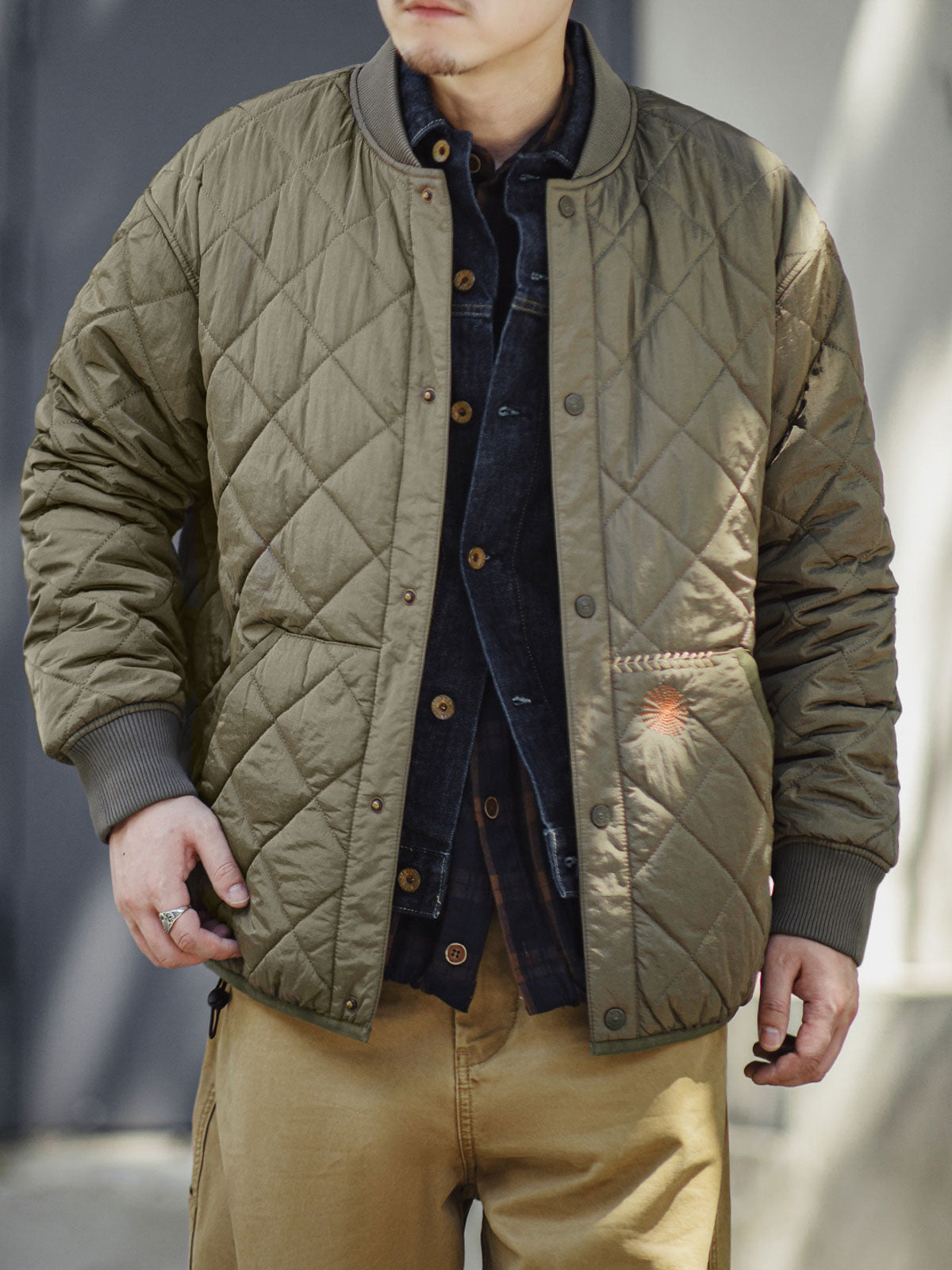 詳細画像: キルティングベースボールジャケットのステッチポケットとオレンジ色の手刺繍風ディテールのクローズアップ。銅製スナップボタンのディテールと、均等に分布した中綿が暖かさを保証。
モデル画像: モデルがキルティングベースボールジャケットデザイン中綿ジャケットを着用している画像。レトロなスタイルと現代的な技術を融合したデザインで、秋冬のカジュアルコーディネートにぴったり。