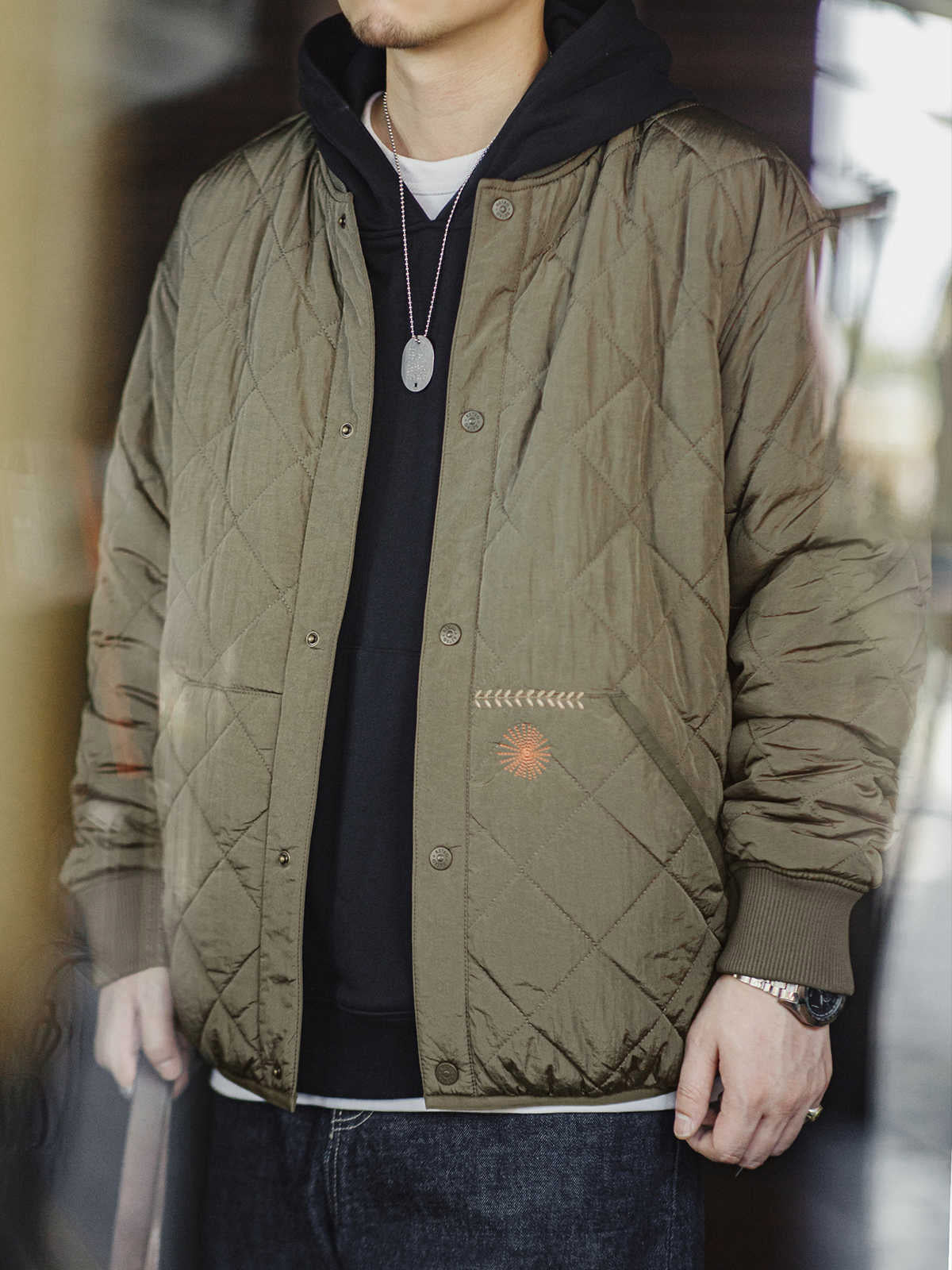詳細画像: キルティングベースボールジャケットのステッチポケットとオレンジ色の手刺繍風ディテールのクローズアップ。銅製スナップボタンのディテールと、均等に分布した中綿が暖かさを保証。
モデル画像: モデルがキルティングベースボールジャケットデザイン中綿ジャケットを着用している画像。レトロなスタイルと現代的な技術を融合したデザインで、秋冬のカジュアルコーディネートにぴったり。