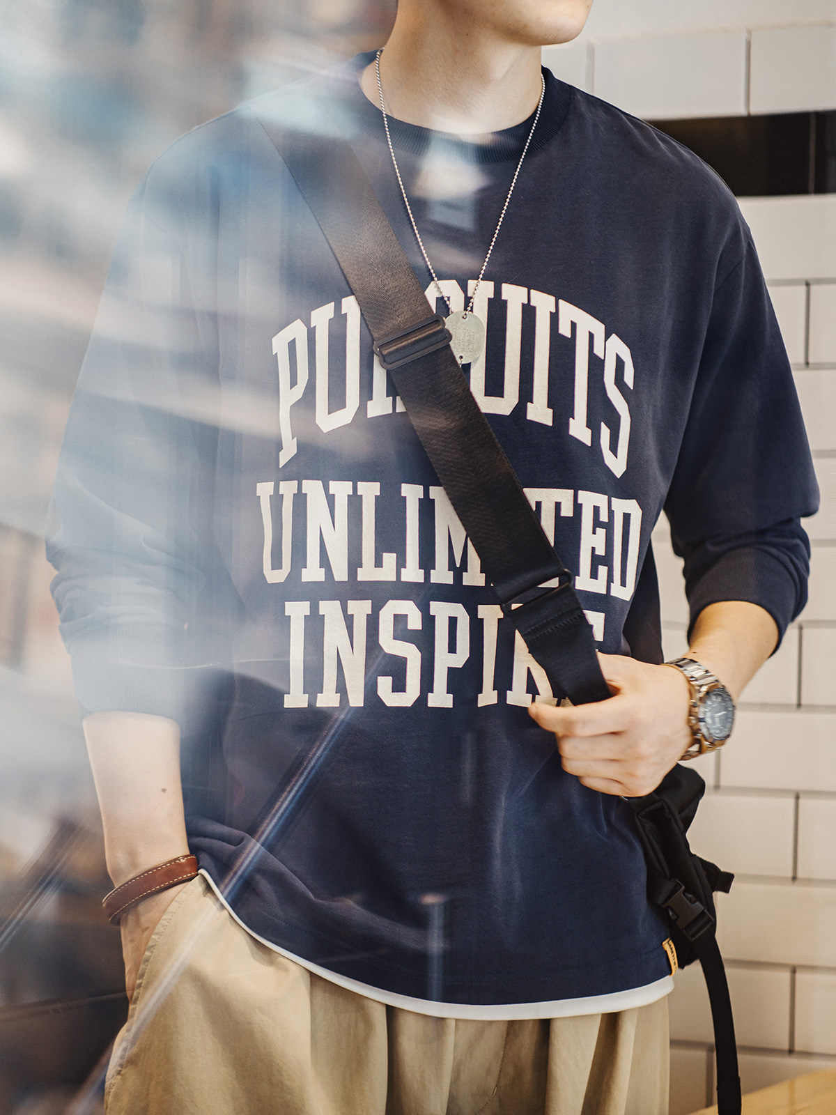 詳細画像
「フロック加工のロゴプリントと起毛素材の滑らかな肌触りをクローズアップ。背面の刺繍アーチロゴや裾のラバープリントタグもディテールとして特徴的。」
モデル画像
「モデルがフロック加工ロゴプリント長袖Tシャツを着用し、ドロップショルダーとクルーネックが特徴のアメリカンストリートスタイルを披露。」