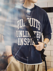 詳細画像
「フロック加工のロゴプリントと起毛素材の滑らかな肌触りをクローズアップ。背面の刺繍アーチロゴや裾のラバープリントタグもディテールとして特徴的。」
モデル画像
「モデルがフロック加工ロゴプリント長袖Tシャツを着用し、ドロップショルダーとクルーネックが特徴のアメリカンストリートスタイルを披露。」