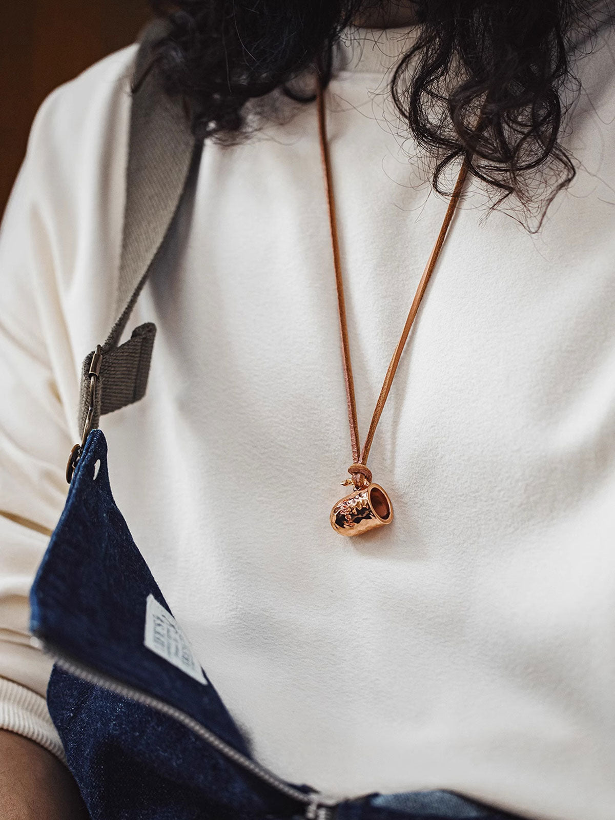 詳細画像
職人の手作業によるハンマーテクスチャーのディテールと、丁寧に彫刻された英文字刻印が印象的な銅カップペンダント。細部にまでこだわりが詰まった表面デザインが、独自のクラフトマンシップを感じさせます。自然な酸化による変化が楽しめる素材感も魅力
モデル画像
ヴィンテージスタイルを演出する銅カップペンダントを身に着けた日常コーディネート例。レザーコードを使用したラフな着こなしや、チェーンと重ね付けした個性的なスタイルで、アクセントとしても存在感を放ちます。ハンドメイドの特別感がデイリールックに溶け込みます
