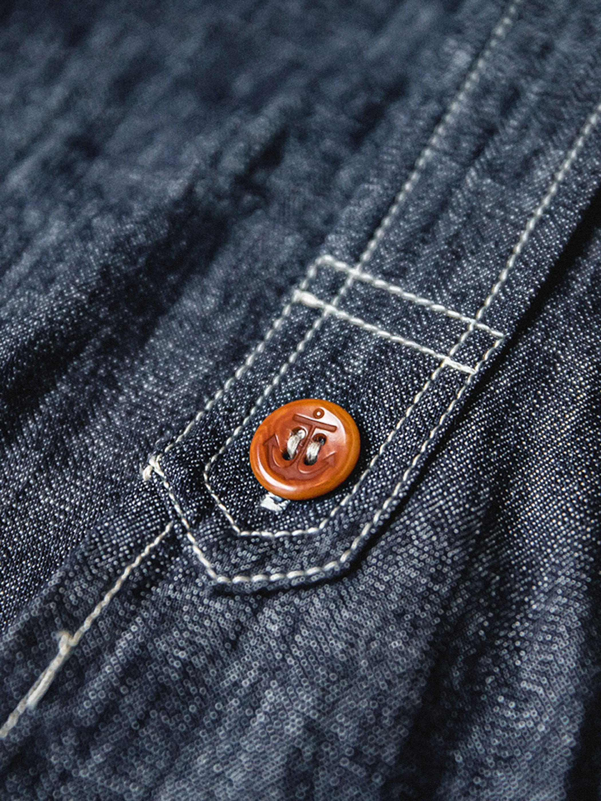 海軍インスパイアのCPOデニムシャツのアンカーボタンのディテールとフラップポケットをクローズアップ。厚手のコットン生地が強調されています。