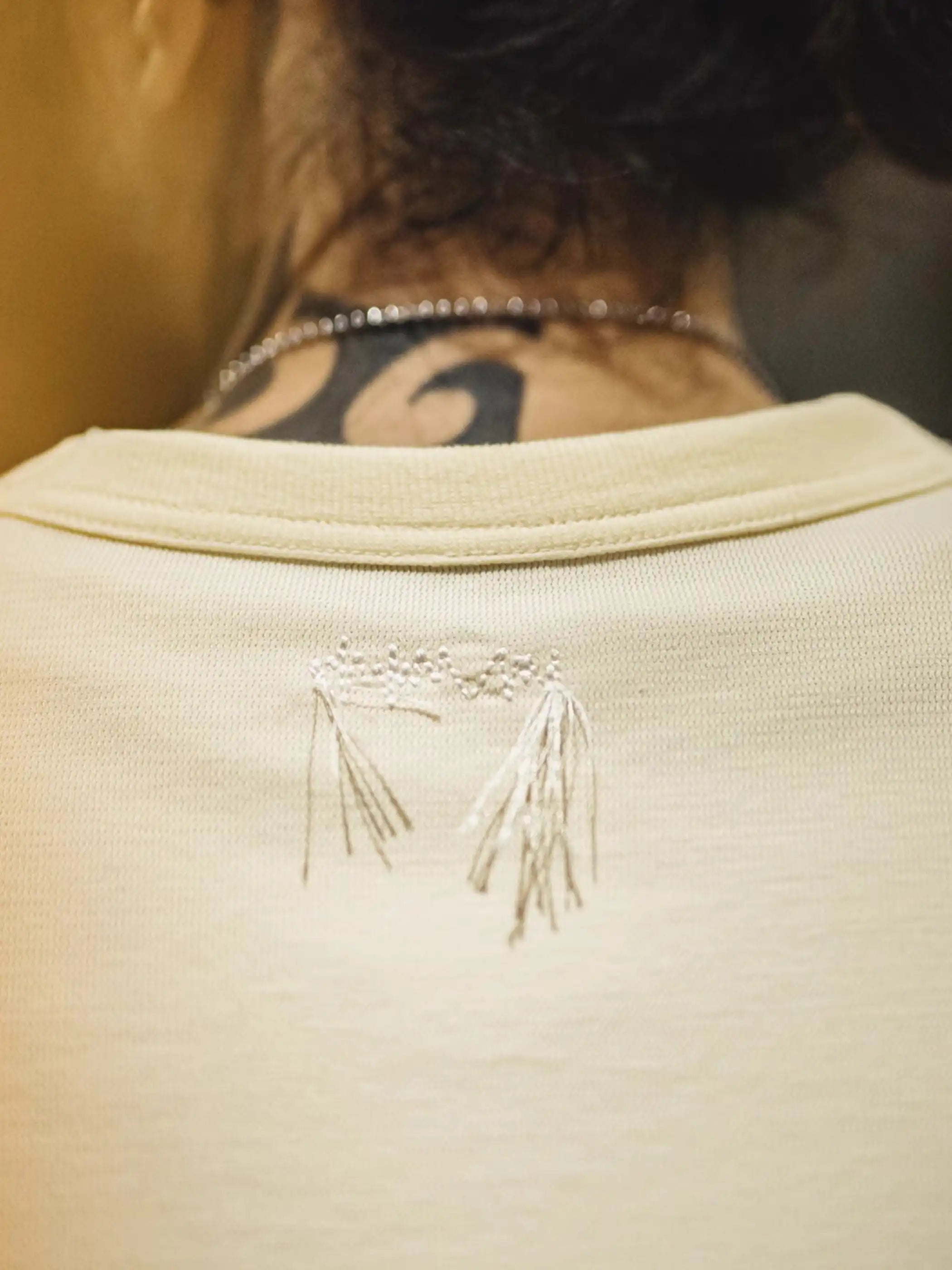 ゆったりとしたドロップショルダーTシャツ、背面上部に同色の波形刺繍が施されている