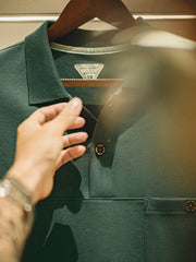 落ち着いた山野グリーンのオーバーサイズポロシャツ、胸ポケットと2粒ボタンの開襟が特徴