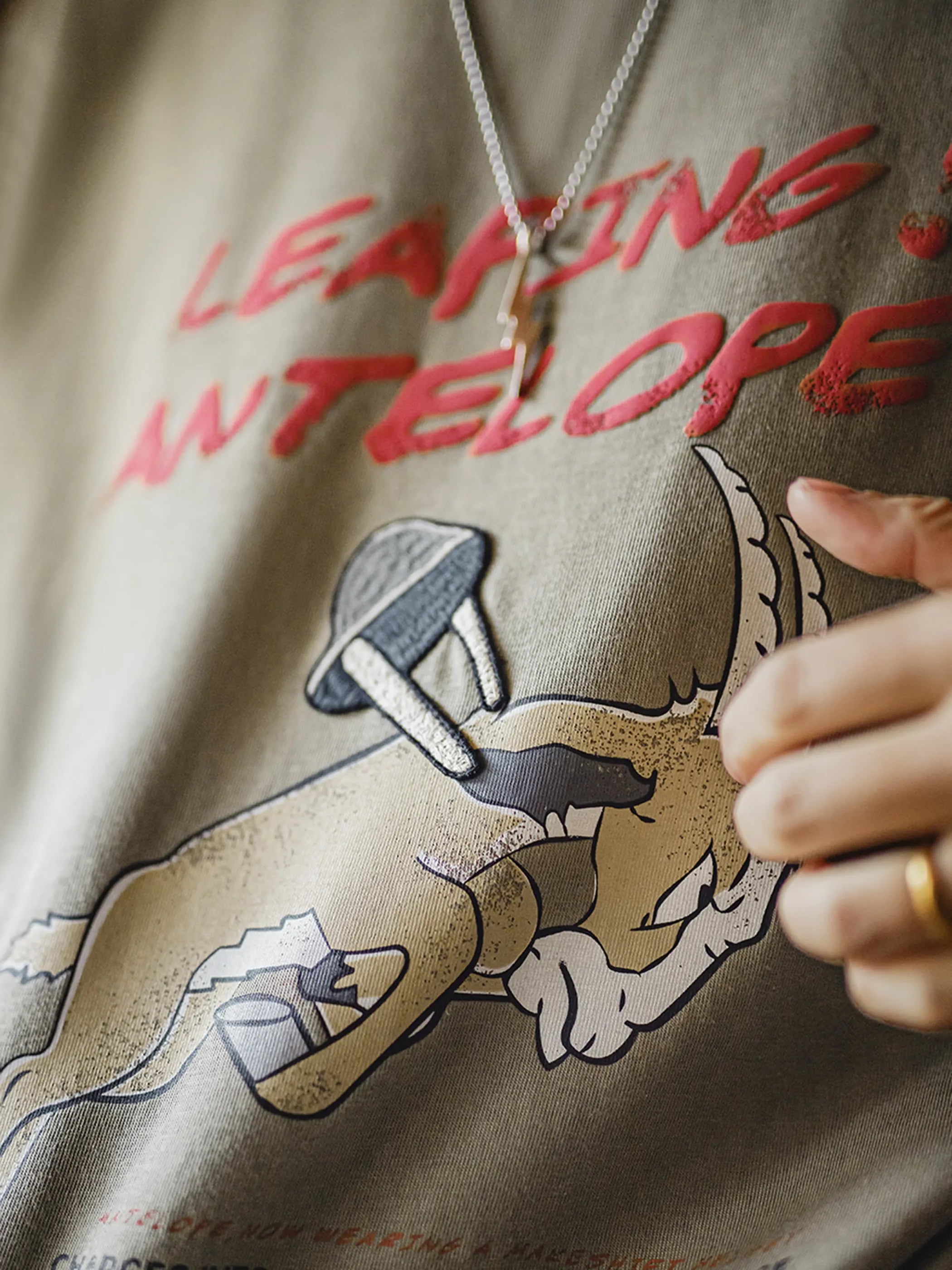 跳ねるアンテロープの刺繍と発泡プリントを施したミリタリーグリーンのTシャツ