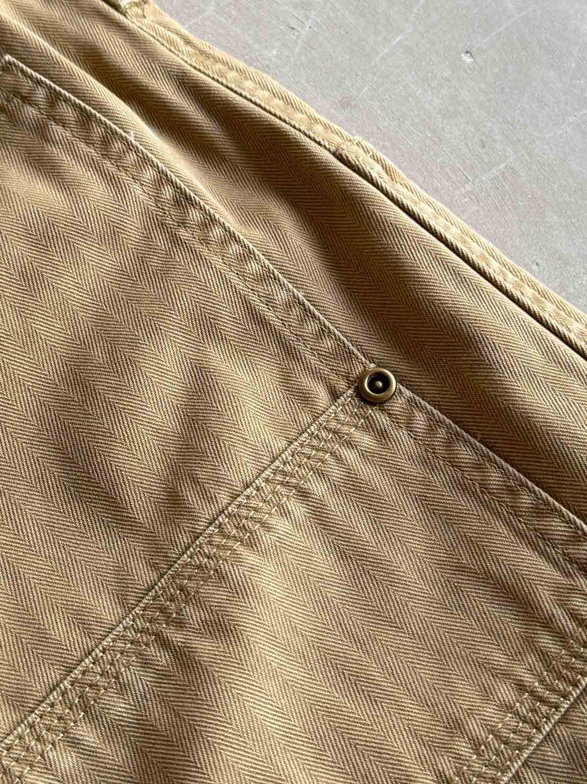 製品画像
「ヘビーウォッシュ加工が施されたヘリンボーン柄コットン素材のアメカジワークパンツ全体イメージ。自然な色褪せやダメージ感、パッチワークディテールが特徴。」
詳細画像
「ヘリンボーン柄コットン素材とヘビーウォッシュ加工によるダメージデザイン、パッチワークディテールをクローズアップ。YKK純銅ジッパーが耐久性を高める。」