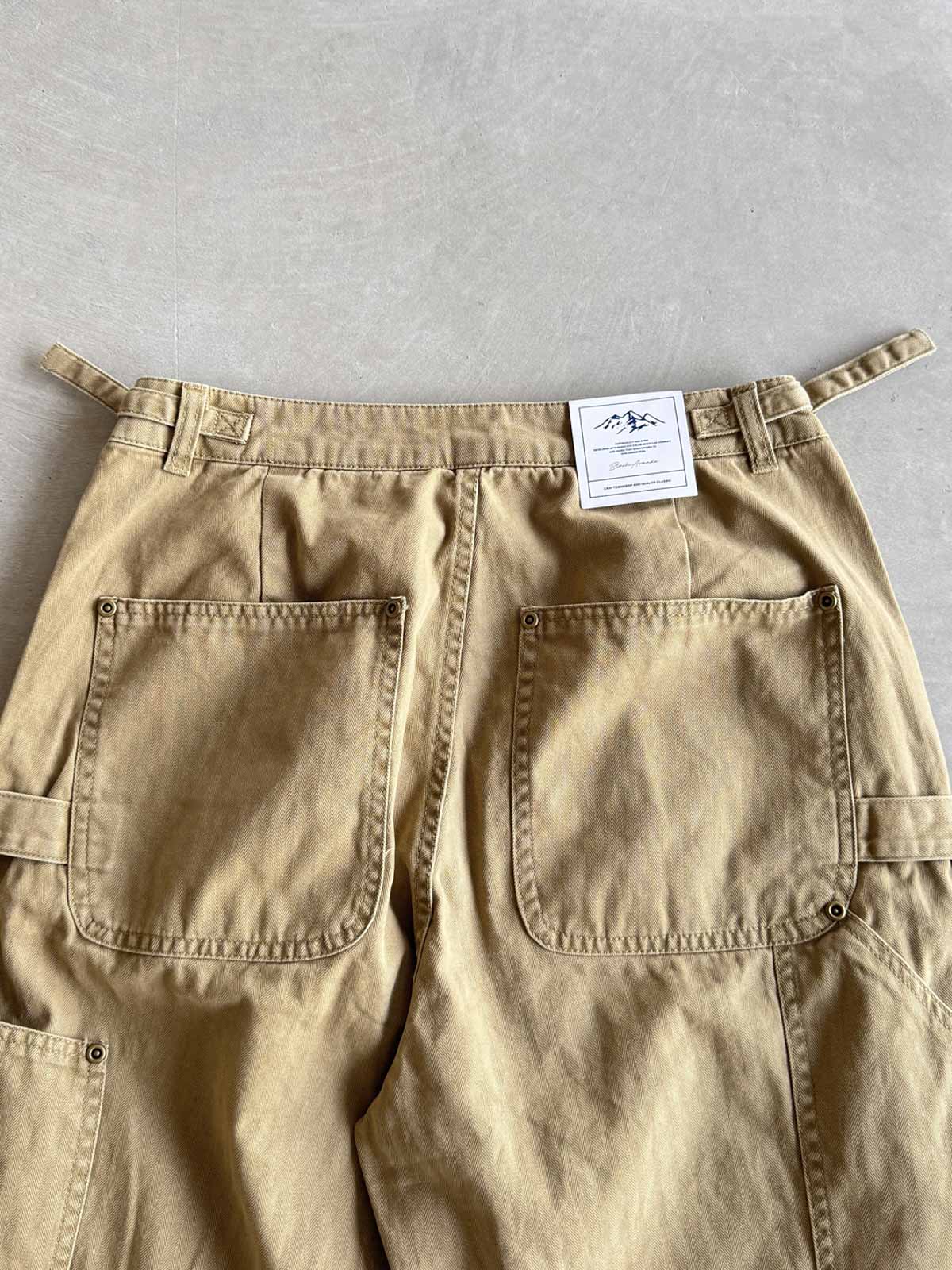 製品画像
「ヘビーウォッシュ加工が施されたヘリンボーン柄コットン素材のアメカジワークパンツ全体イメージ。自然な色褪せやダメージ感、パッチワークディテールが特徴。」
詳細画像
「ヘリンボーン柄コットン素材とヘビーウォッシュ加工によるダメージデザイン、パッチワークディテールをクローズアップ。YKK純銅ジッパーが耐久性を高める。」