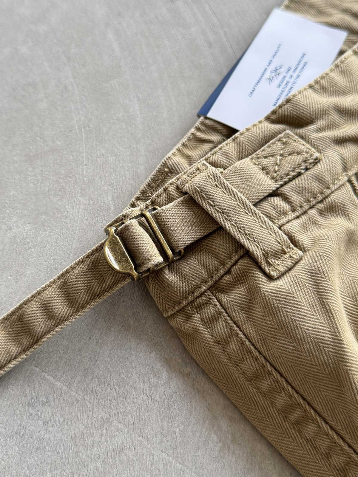 製品画像
「ヘビーウォッシュ加工が施されたヘリンボーン柄コットン素材のアメカジワークパンツ全体イメージ。自然な色褪せやダメージ感、パッチワークディテールが特徴。」
詳細画像
「ヘリンボーン柄コットン素材とヘビーウォッシュ加工によるダメージデザイン、パッチワークディテールをクローズアップ。YKK純銅ジッパーが耐久性を高める。」