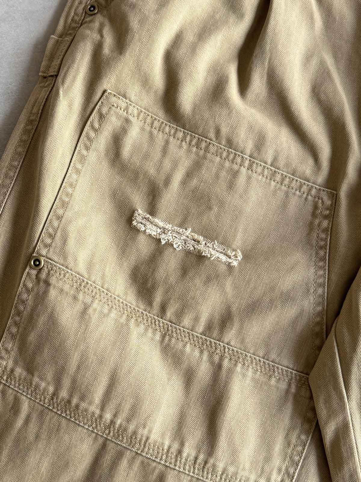 製品画像
「ヘビーウォッシュ加工が施されたヘリンボーン柄コットン素材のアメカジワークパンツ全体イメージ。自然な色褪せやダメージ感、パッチワークディテールが特徴。」
詳細画像
「ヘリンボーン柄コットン素材とヘビーウォッシュ加工によるダメージデザイン、パッチワークディテールをクローズアップ。YKK純銅ジッパーが耐久性を高める。」