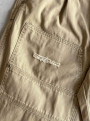 製品画像
「ヘビーウォッシュ加工が施されたヘリンボーン柄コットン素材のアメカジワークパンツ全体イメージ。自然な色褪せやダメージ感、パッチワークディテールが特徴。」
詳細画像
「ヘリンボーン柄コットン素材とヘビーウォッシュ加工によるダメージデザイン、パッチワークディテールをクローズアップ。YKK純銅ジッパーが耐久性を高める。」