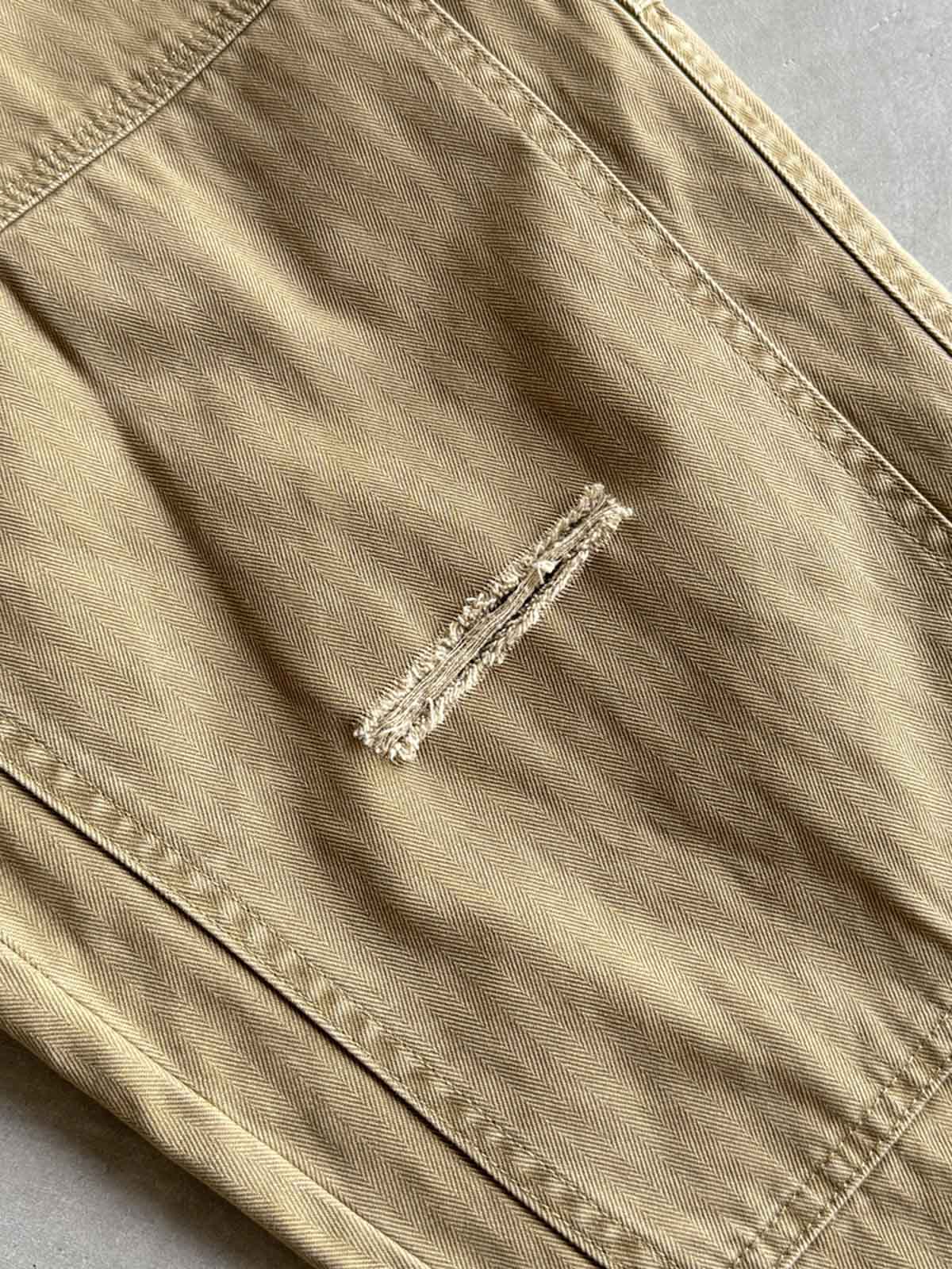 製品画像
「ヘビーウォッシュ加工が施されたヘリンボーン柄コットン素材のアメカジワークパンツ全体イメージ。自然な色褪せやダメージ感、パッチワークディテールが特徴。」
詳細画像
「ヘリンボーン柄コットン素材とヘビーウォッシュ加工によるダメージデザイン、パッチワークディテールをクローズアップ。YKK純銅ジッパーが耐久性を高める。」