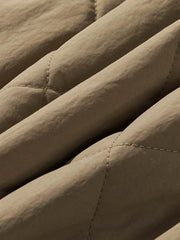 製品画像:クラシックなVネックデザインのキルティングチェック柄中綿ジャケット、100%ナイロン素材で防風性と耐裂性に優れた実用的なデザイン。秋冬に最適なシンプルで深みのあるスタイル。
詳細画像:精緻なチェック柄キルティング加工のディテール、耐久性と保温性を高める素材選び。中綿使用で軽量ながら適度な保温性を提供。