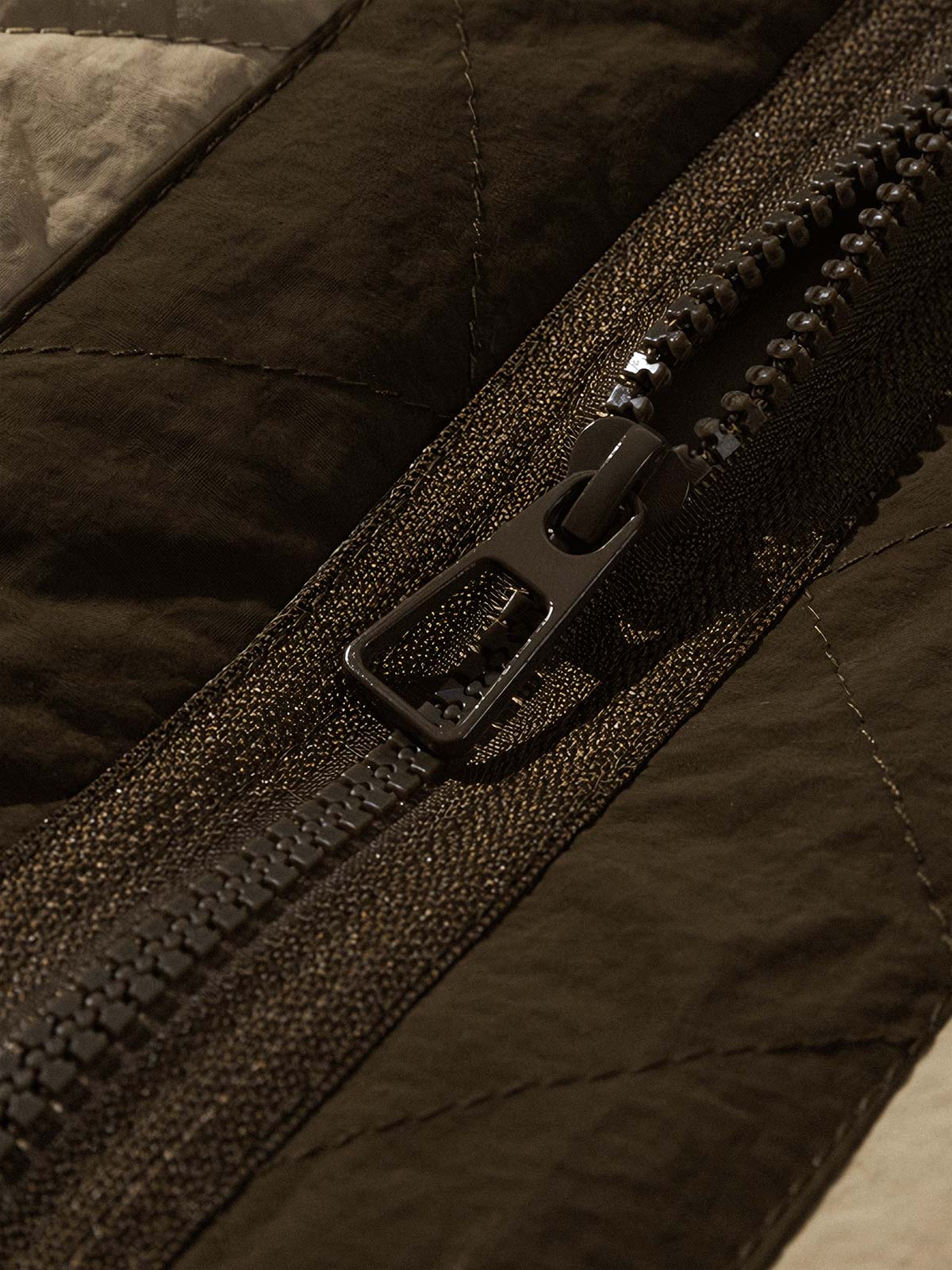 製品画像:クラシックなVネックデザインのキルティングチェック柄中綿ジャケット、100%ナイロン素材で防風性と耐裂性に優れた実用的なデザイン。秋冬に最適なシンプルで深みのあるスタイル。
詳細画像:精緻なチェック柄キルティング加工のディテール、耐久性と保温性を高める素材選び。中綿使用で軽量ながら適度な保温性を提供。