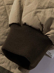 製品画像:クラシックなVネックデザインのキルティングチェック柄中綿ジャケット、100%ナイロン素材で防風性と耐裂性に優れた実用的なデザイン。秋冬に最適なシンプルで深みのあるスタイル。
詳細画像:精緻なチェック柄キルティング加工のディテール、耐久性と保温性を高める素材選び。中綿使用で軽量ながら適度な保温性を提供。