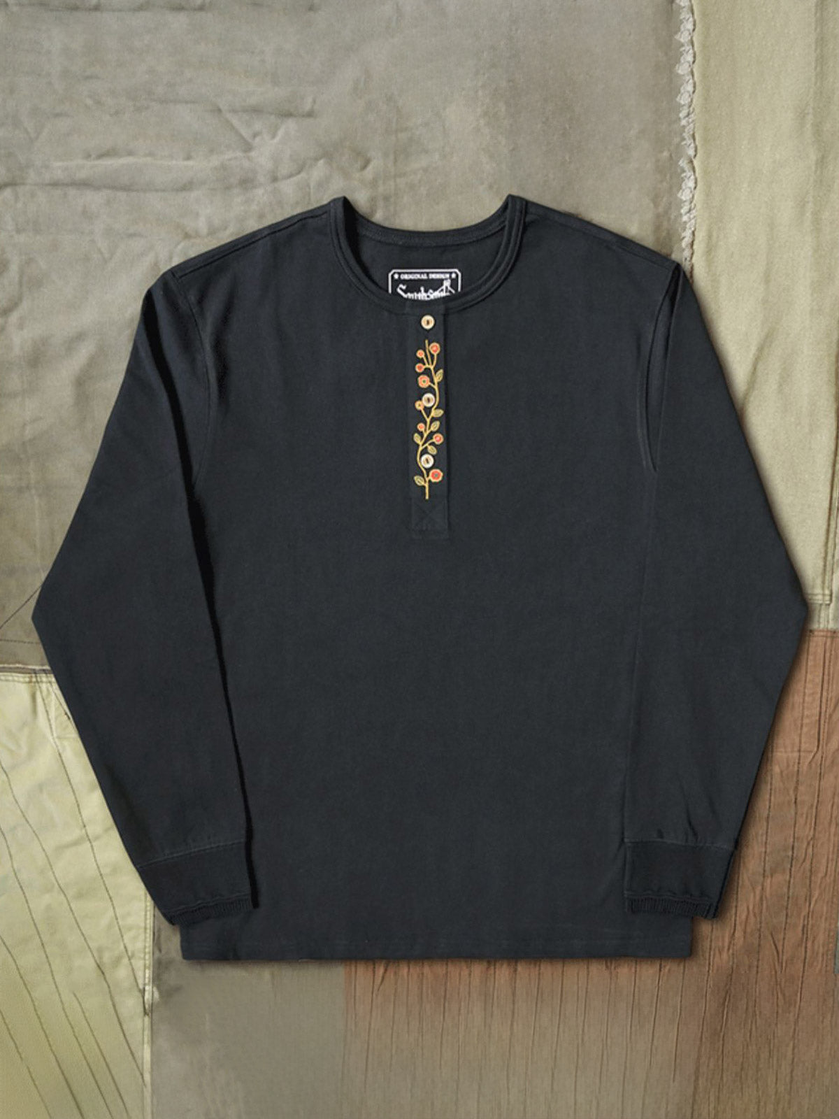 製品画像
クラシックな刺繍入りデザインの改良型ヴィンテージヘンリーネック 長袖Tシャツの正面全体画像。高品質なアメリカ産ピマコットン素材を使用した一着。
詳細画像
刺繍入りの近似色前立てとダブルステッチ仕上げ、リブ仕様の袖口ディテールをクローズアップした画像。美しい縫製と耐久性が特徴。