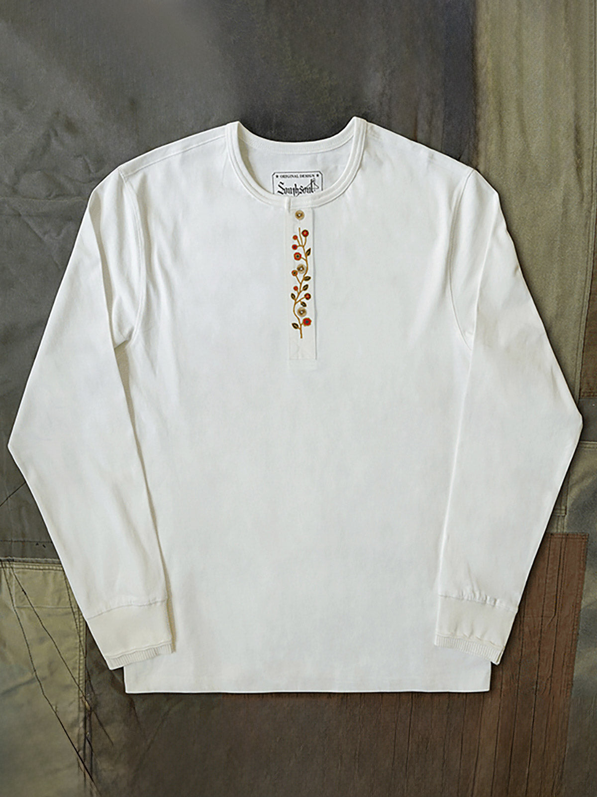 製品画像
クラシックな刺繍入りデザインの改良型ヴィンテージヘンリーネック 長袖Tシャツの正面全体画像。高品質なアメリカ産ピマコットン素材を使用した一着。
詳細画像
刺繍入りの近似色前立てとダブルステッチ仕上げ、リブ仕様の袖口ディテールをクローズアップした画像。美しい縫製と耐久性が特徴。