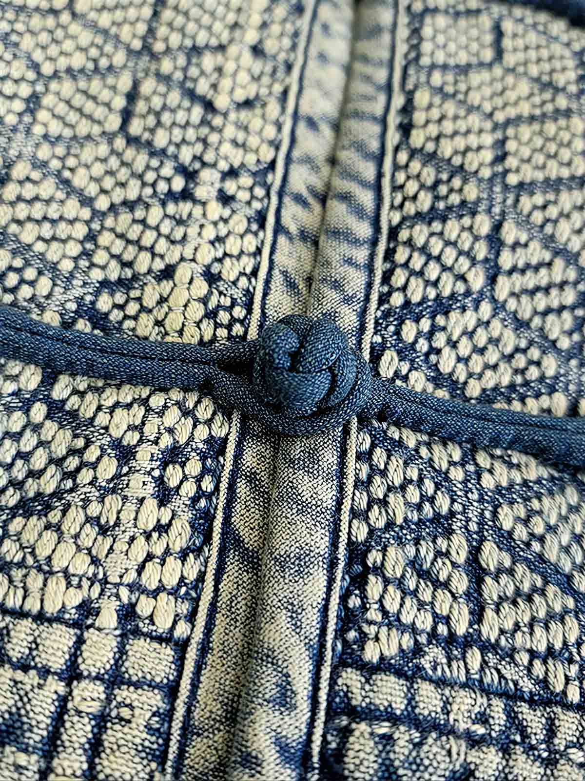 製品画像: 藍染め刺子織りピースワークスタンドカラージャケット全体写真。立ち襟とチャイナボタンが特徴の伝統とモダンが融合したデザイン。
詳細画像: 刺子織りの繊細なテクスチャと藍染めの深みある色合いを強調したディテール写真。水洗抜染加工による個性的な風合いを表現。