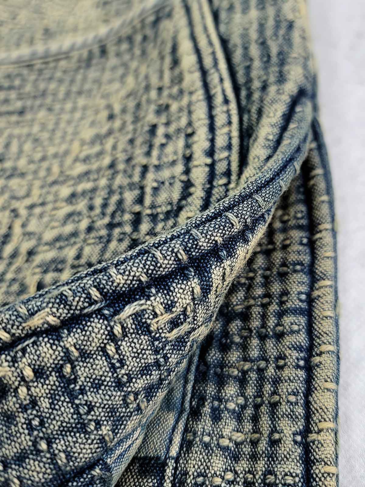 製品画像: 藍染め刺子織りピースワークスタンドカラージャケット全体写真。立ち襟とチャイナボタンが特徴の伝統とモダンが融合したデザイン。
詳細画像: 刺子織りの繊細なテクスチャと藍染めの深みある色合いを強調したディテール写真。水洗抜染加工による個性的な風合いを表現。