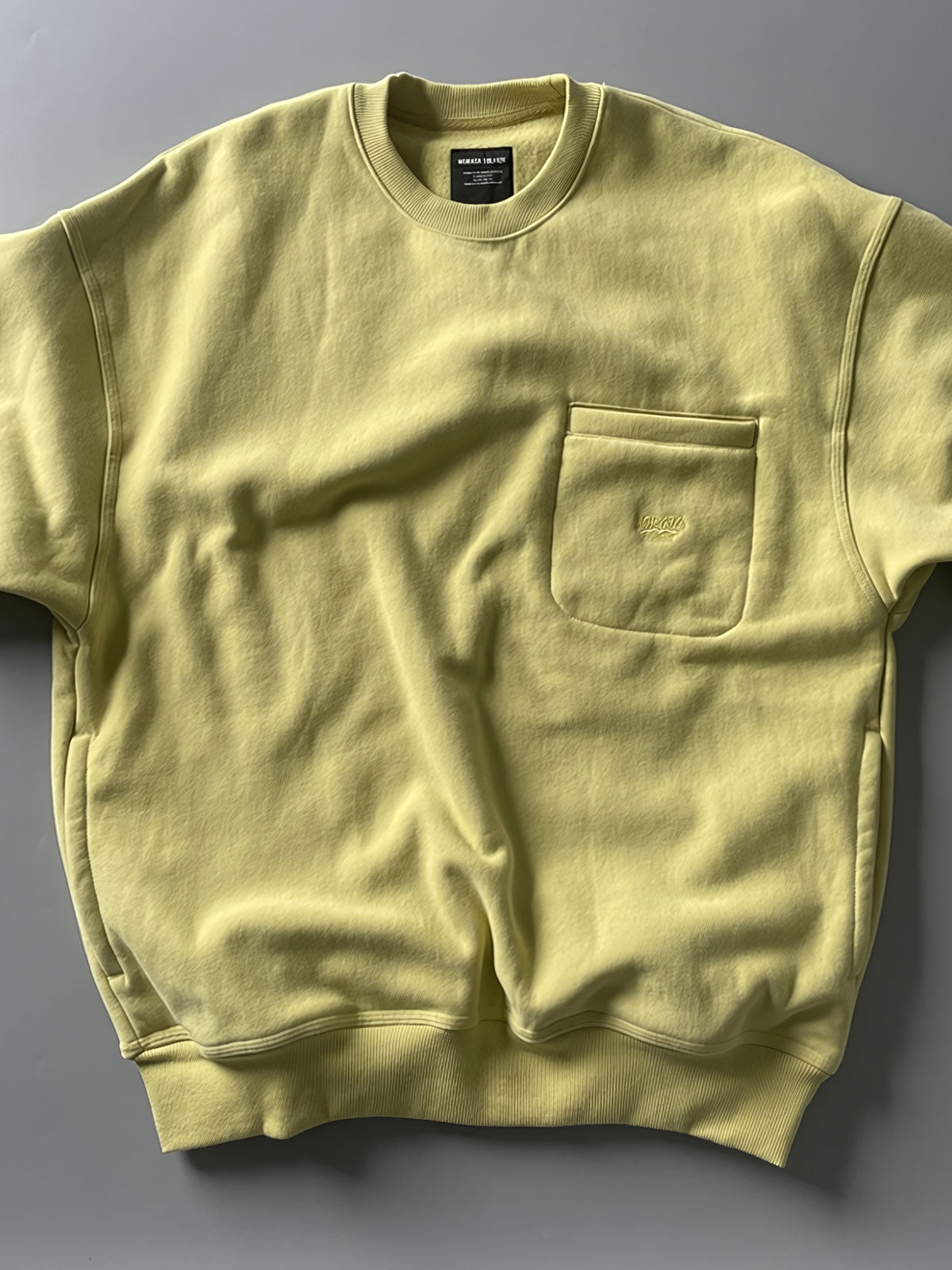 製品画像: ライムイエロー起毛裏起毛スウェットシャツの正面画像、快適で暖かいデザインが特徴。
詳細画像: 胸ポケットと起毛生地のディテール画像、柔らかな質感が際立つ。