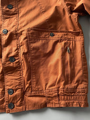 製品画像: オレンジカラーのダブルスタンドカラーワークジャケットの正面画像、実用的でスタイリッシュなデザインが特徴。
詳細画像: 袖部のジッパーポケットとスタンドカラーデザインのディテール画像、ワークスタイルを強調。