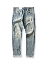 製品画像: ヴィンテージ風破れ加工・パッチ付きデニムパンツ全体画像、ライトブルーのウォッシュ加工とストリート感あふれるデザイン
詳細画像: 破れ加工、パッチディテールのクローズアップ、ヴィンテージ風デニムパンツのディテール、セルビッジデザインが特徴