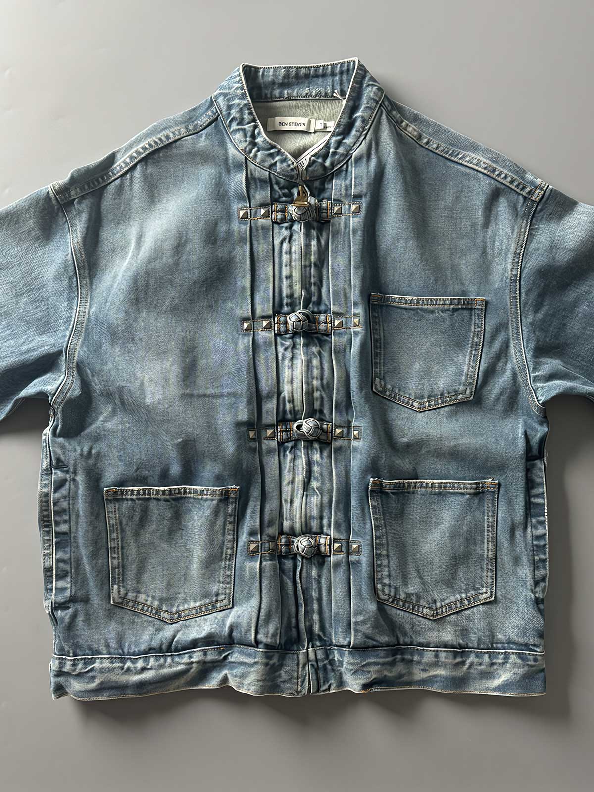 製品画像: チャイニーズボタンヴィンテージデニムジャケットの正面画像、東洋と西洋のデザインが融合したユニークなスタイル。
詳細画像: チャイニーズボタンとウォッシュ加工のディテール画像、質感を際立たせる。
