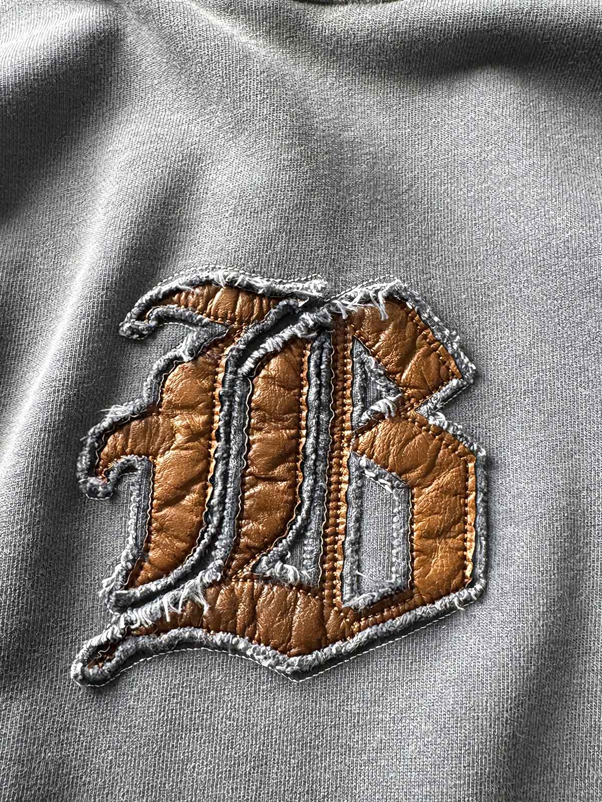 製品画像: ヴィンテージ加工のピグメント染めフード付きパーカーの全体画像、ヘビーウェイトで快適な着心地。
詳細画像: パーカーのピグメント染めとロゴ刺繍のディテール画像、独特の風合いを強調。