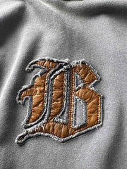 製品画像: ヴィンテージ加工のピグメント染めフード付きパーカーの全体画像、ヘビーウェイトで快適な着心地。
詳細画像: パーカーのピグメント染めとロゴ刺繍のディテール画像、独特の風合いを強調。