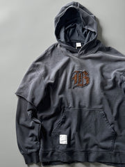 製品画像: ヴィンテージ加工のピグメント染めフード付きパーカーの全体画像、ヘビーウェイトで快適な着心地。
詳細画像: パーカーのピグメント染めとロゴ刺繍のディテール画像、独特の風合いを強調。