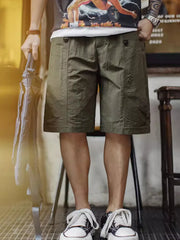 ミリタリーグリーンのショーツ、両腿に大きな風琴ポケットとウェビングストラップ付き
