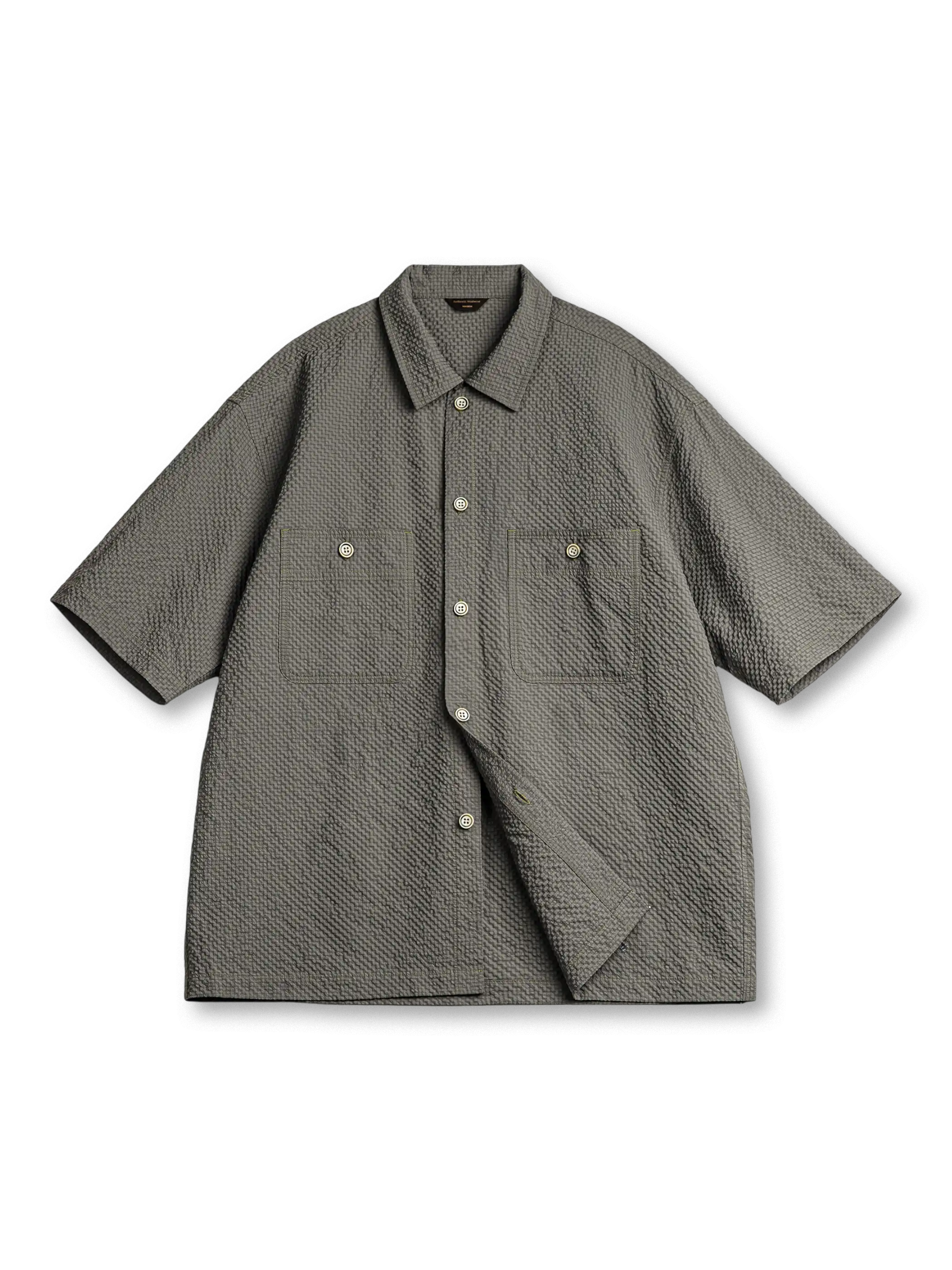 軽量シアサッカー生地を使用した2ポケットワークシャツ。小さめ襟と5ボタン仕様、背面にレーザー木製プレートと琥珀ボタンがアクセントの涼しげでモダンなデザイン。