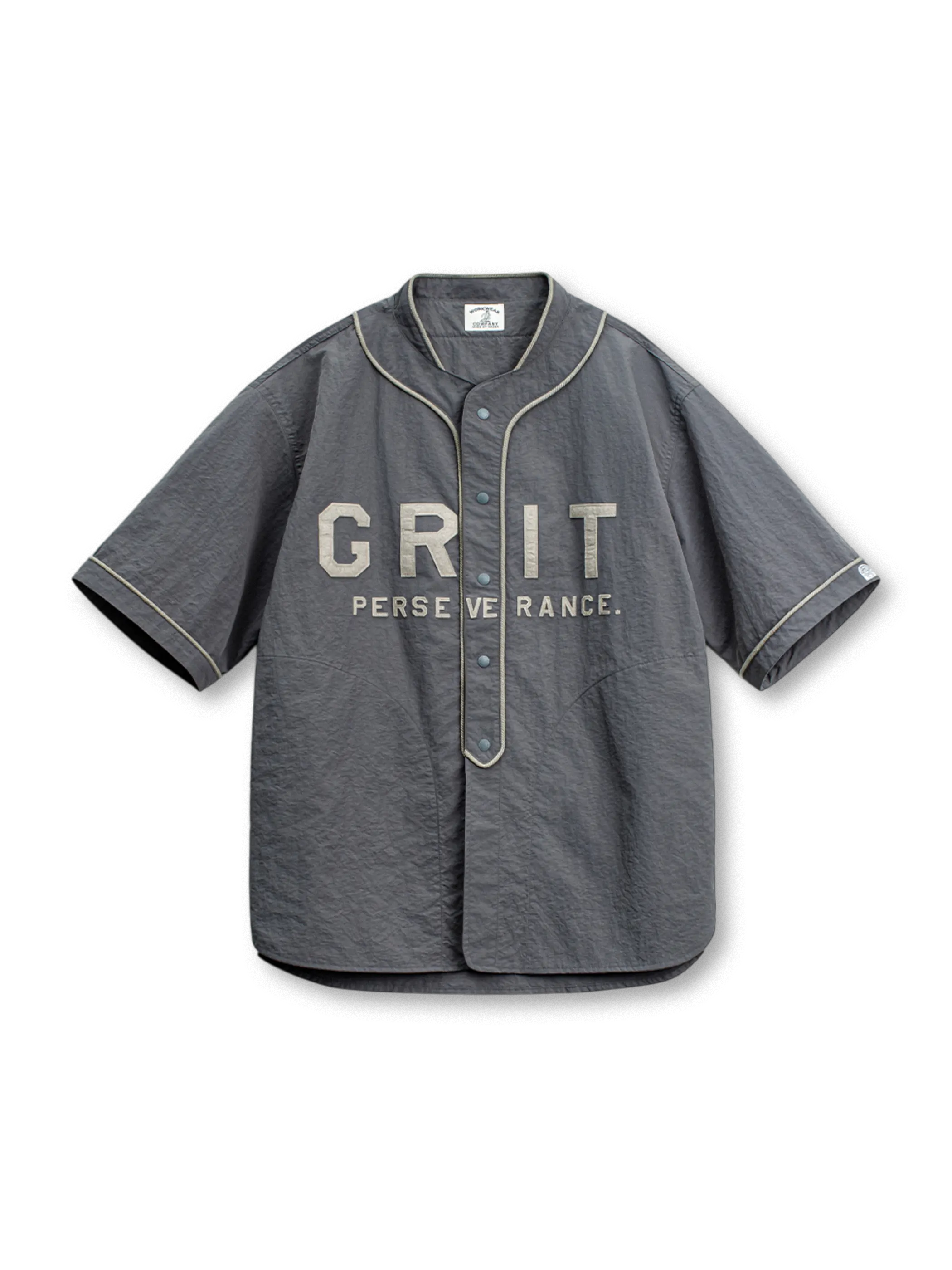 「GRIT PERSEVERANCE」パッチとホログラムボタンが特徴の90年代風軽量ベースボールシャツ。