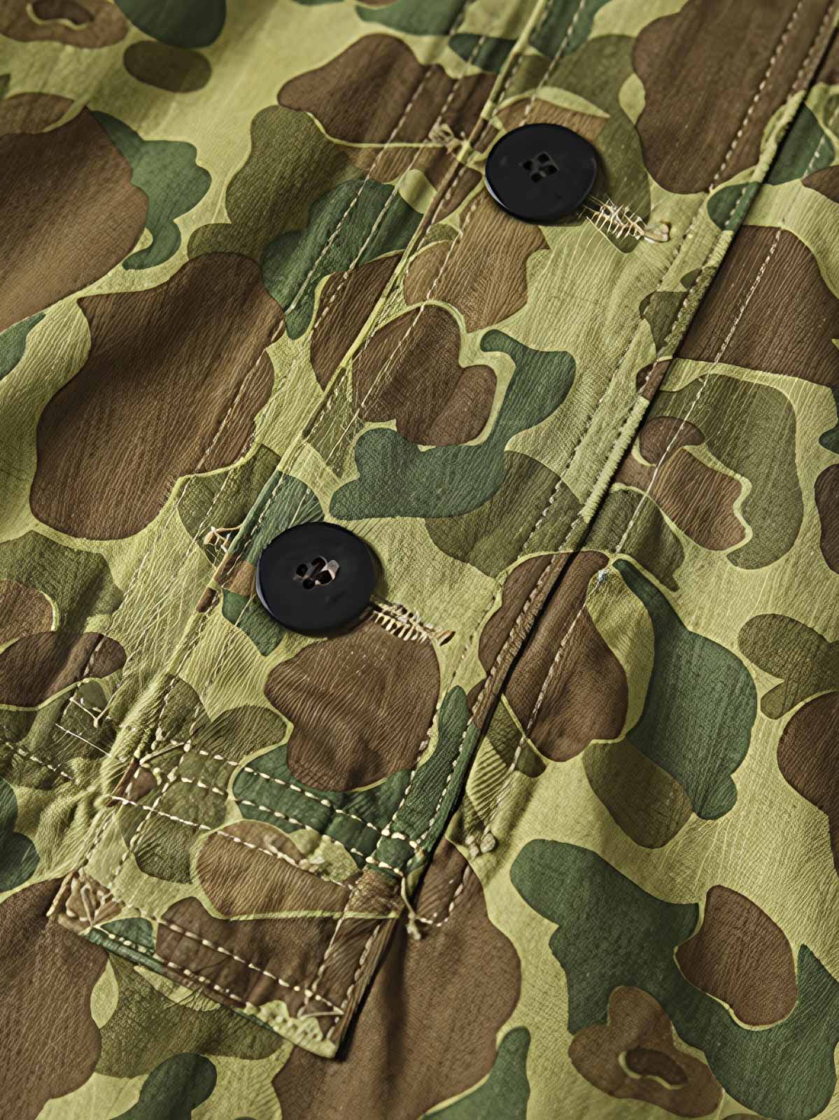 製品画像: 迷彩柄ツイルデニム生地の砲兵防護プルオーバーパーカー復刻バージョンの正面画像。
詳細画像: 大きなフードと三層前立てデザインのディテール特写。機能性とヴィンテージ感が際立つディテール。