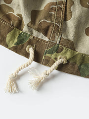 製品画像: 迷彩柄ツイルデニム生地の砲兵防護プルオーバーパーカー復刻バージョンの正面画像。
詳細画像: 大きなフードと三層前立てデザインのディテール特写。機能性とヴィンテージ感が際立つディテール。