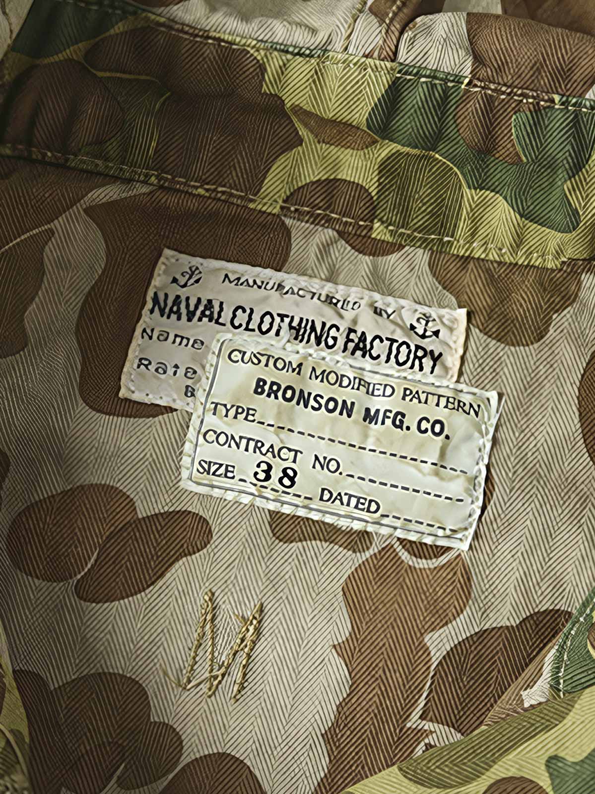 製品画像: 迷彩柄ツイルデニム生地の砲兵防護プルオーバーパーカー復刻バージョンの正面画像。
詳細画像: 大きなフードと三層前立てデザインのディテール特写。機能性とヴィンテージ感が際立つディテール。